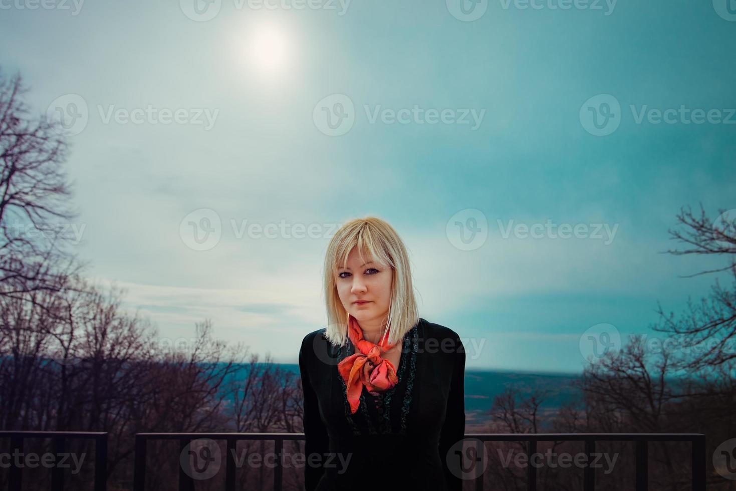 Blonde woman with red scarf and black shirt in the forest looking at the camera. Springtime, outdoor portrait. photo