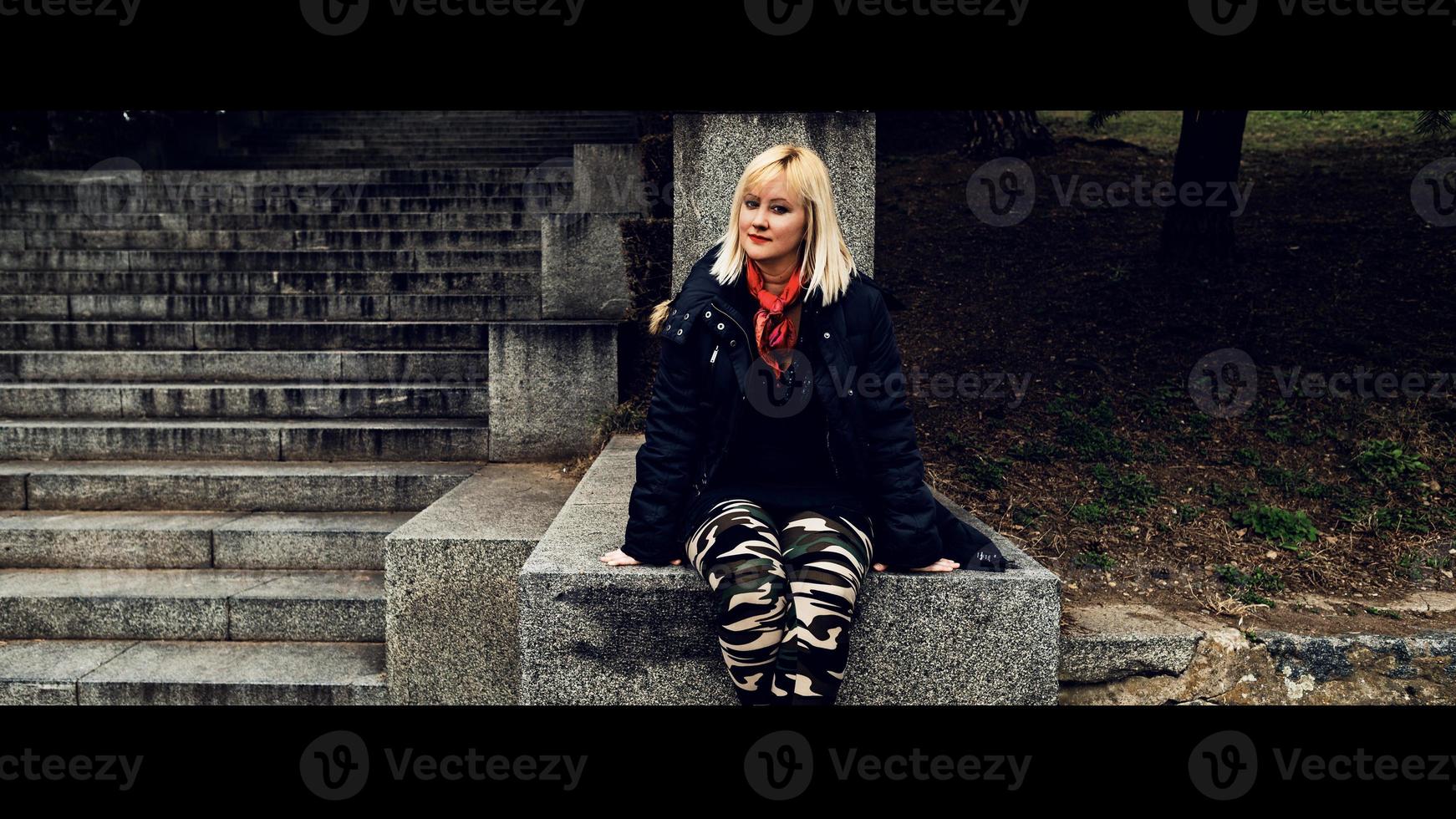 A blonde woman with red scarf sitting on the stone stairs and looking at the camera. photo