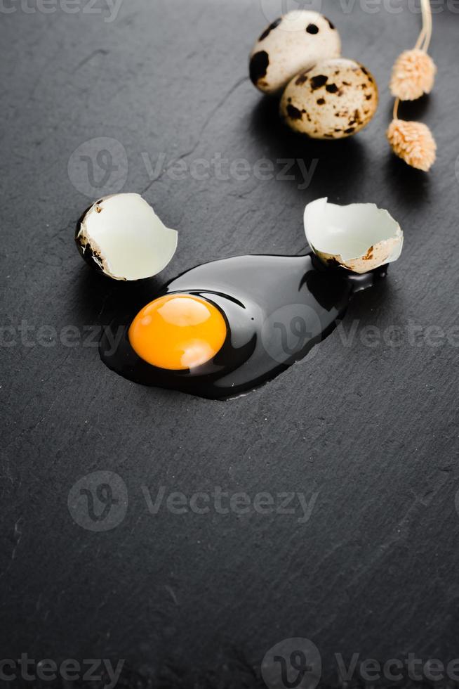 Quail eggs on black stone background, broken, cracked quail egg, yolk of quail egg. Organic product. photo