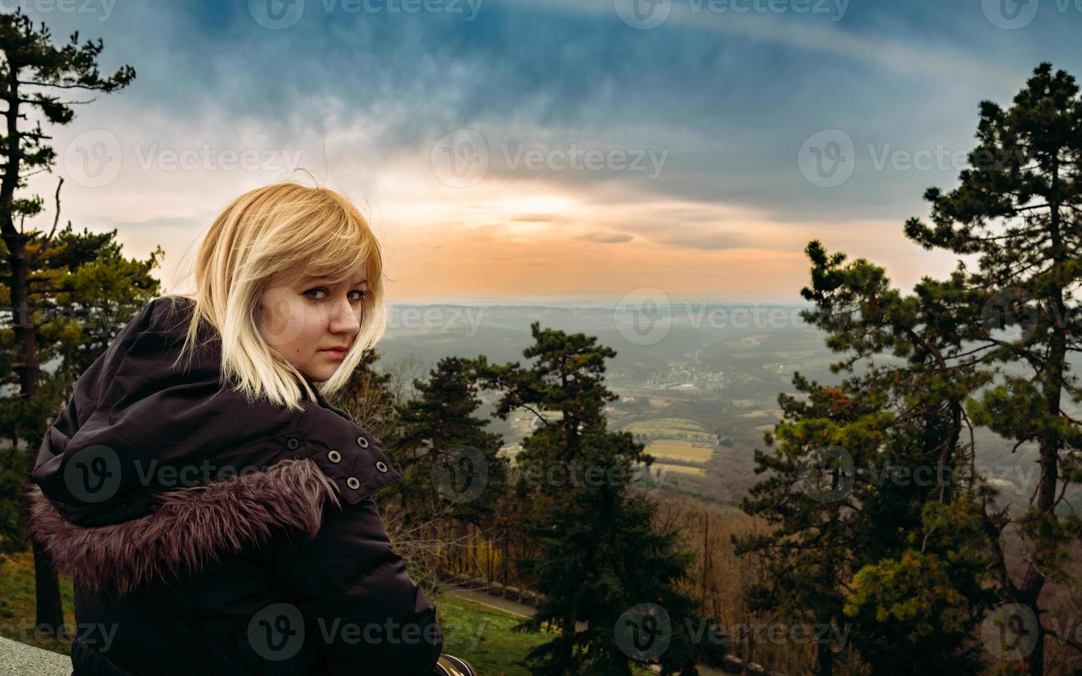 A woman sitting on the edge of forest gate, enjoying the beautiful sunset view, mountain panoramic landscape view. photo