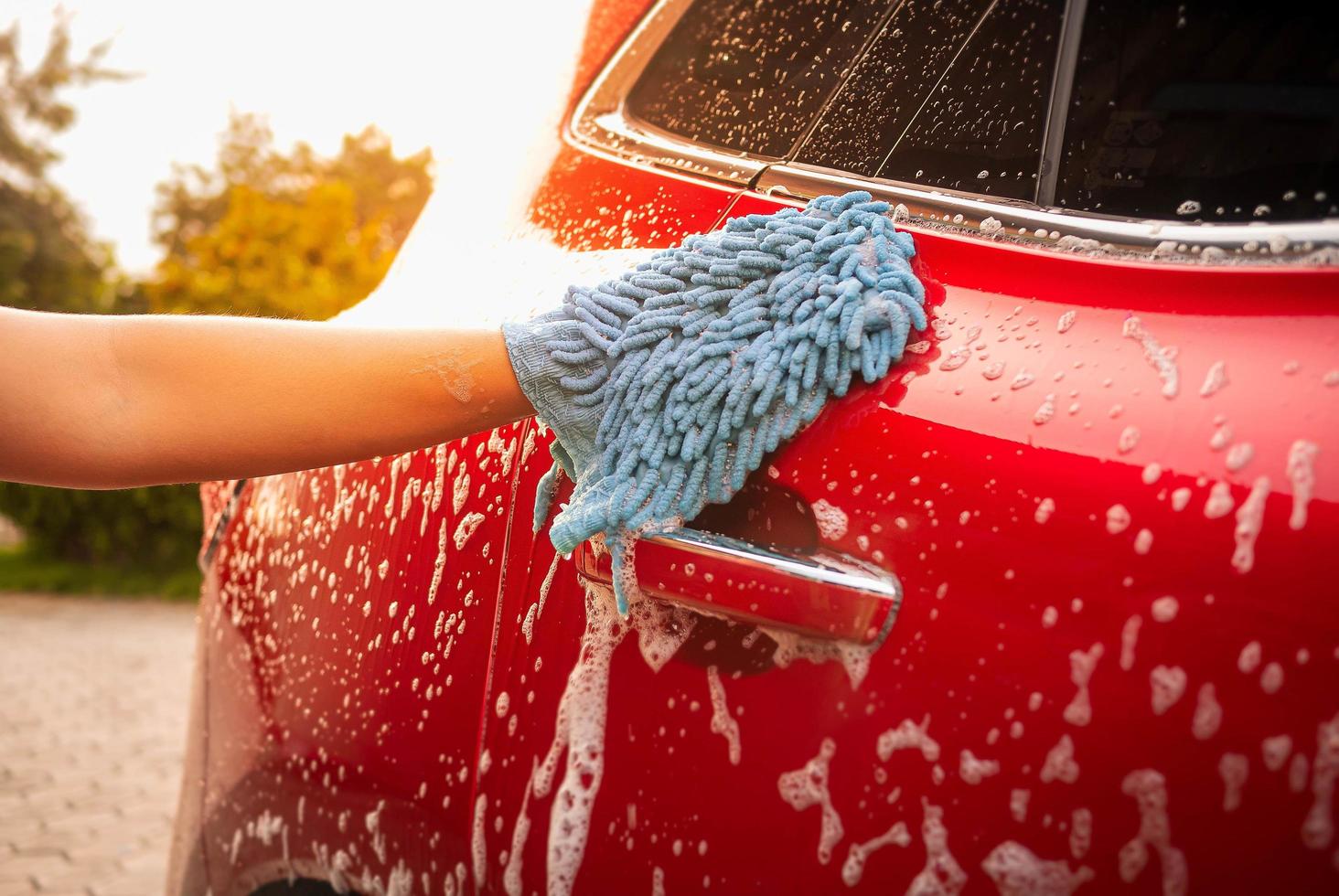 Cerca de la mano está lavando el coche por guante con jabón de burbujas al aire libre. foto