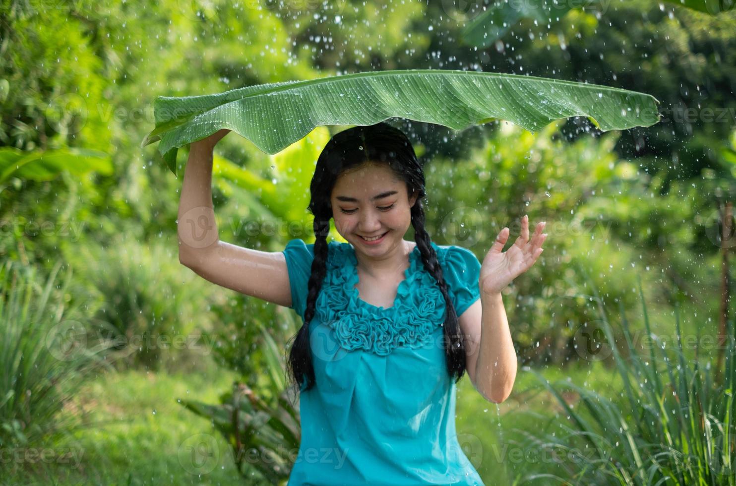 Retrato de una joven mujer asiática con cabello negro sosteniendo una hoja de plátano en la lluvia en el fondo del jardín verde foto