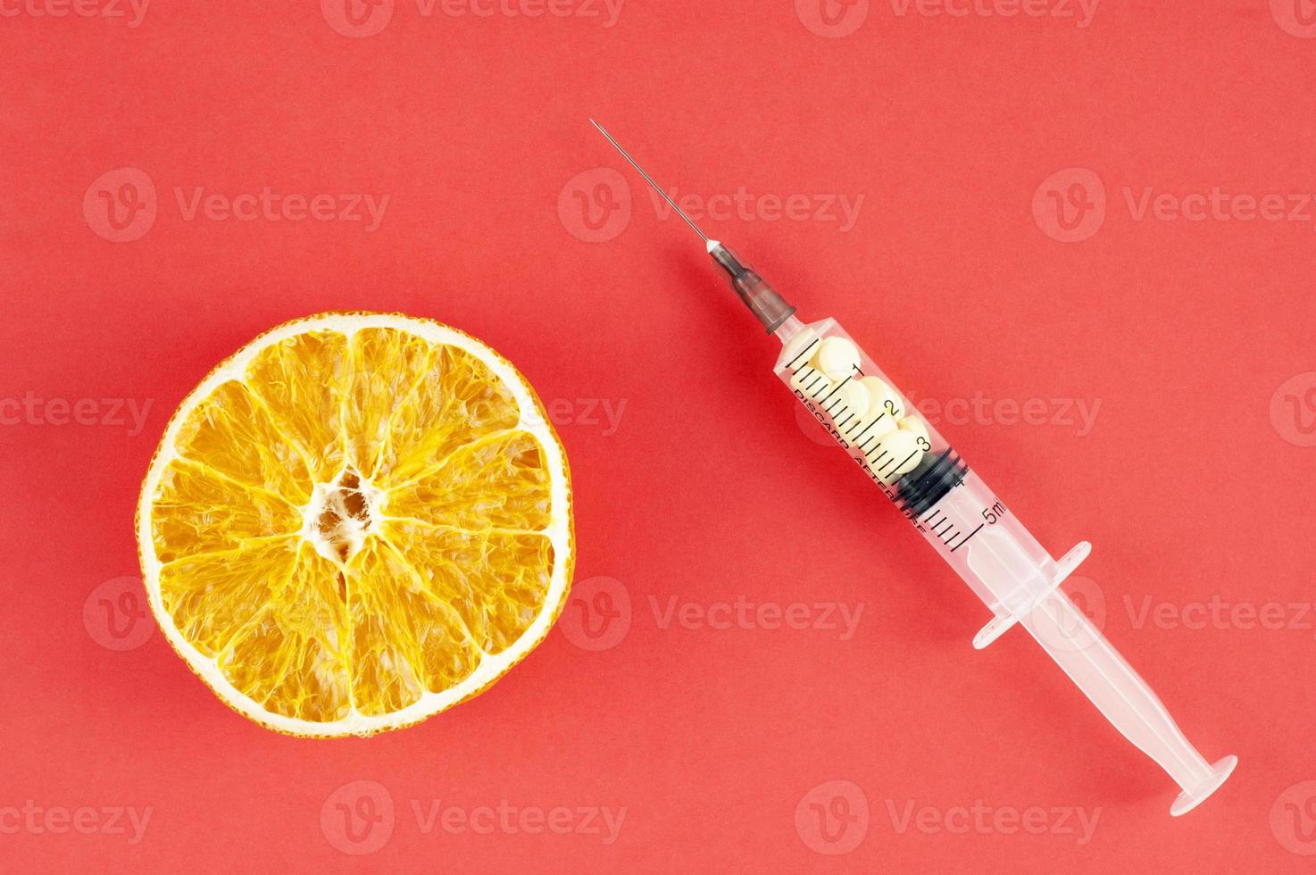 Naranja seca y una jeringa con pastillas de color amarillo sobre fondo rojo. foto