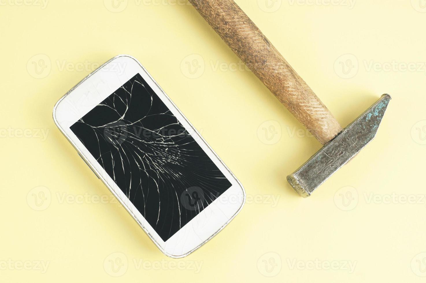 A cell phone with cracked screen and a hammer on brown background photo