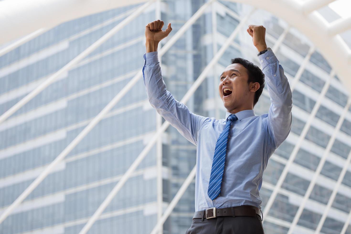 Businessman holds up hand after successful business and standing outdoors with office building in the background photo