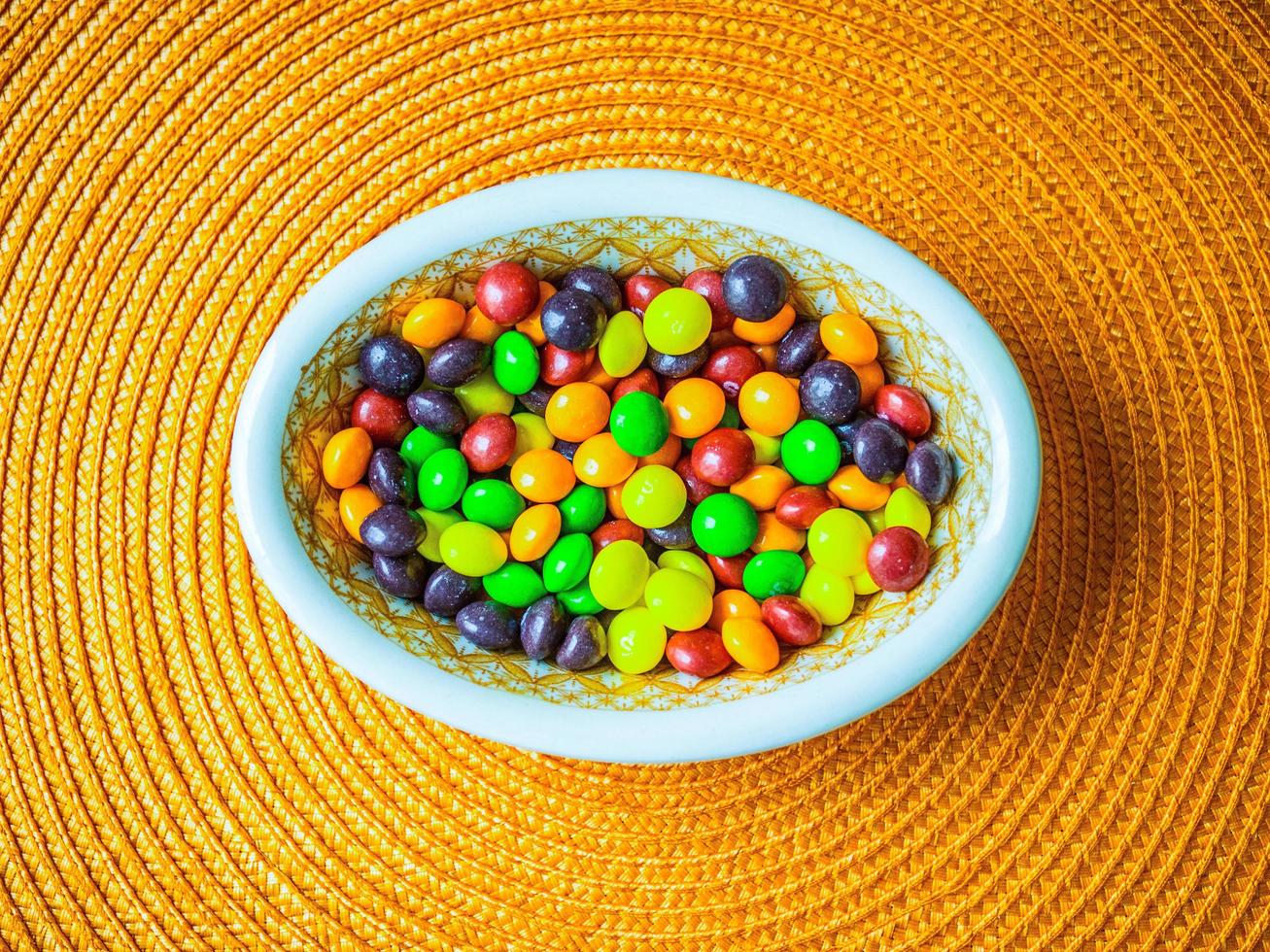 A bowl of candies on an orange placemat. photo