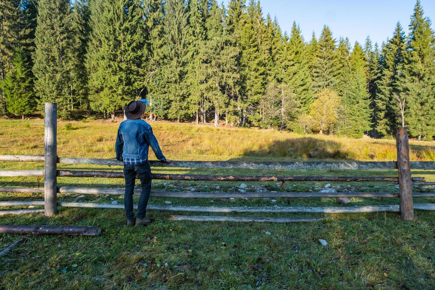 Cowboy in a denim jacket and hat near the fence in the mountains photo