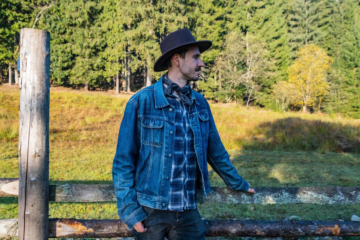 vaquero en una chaqueta de mezclilla y un sombrero cerca de la valla en las montañas foto