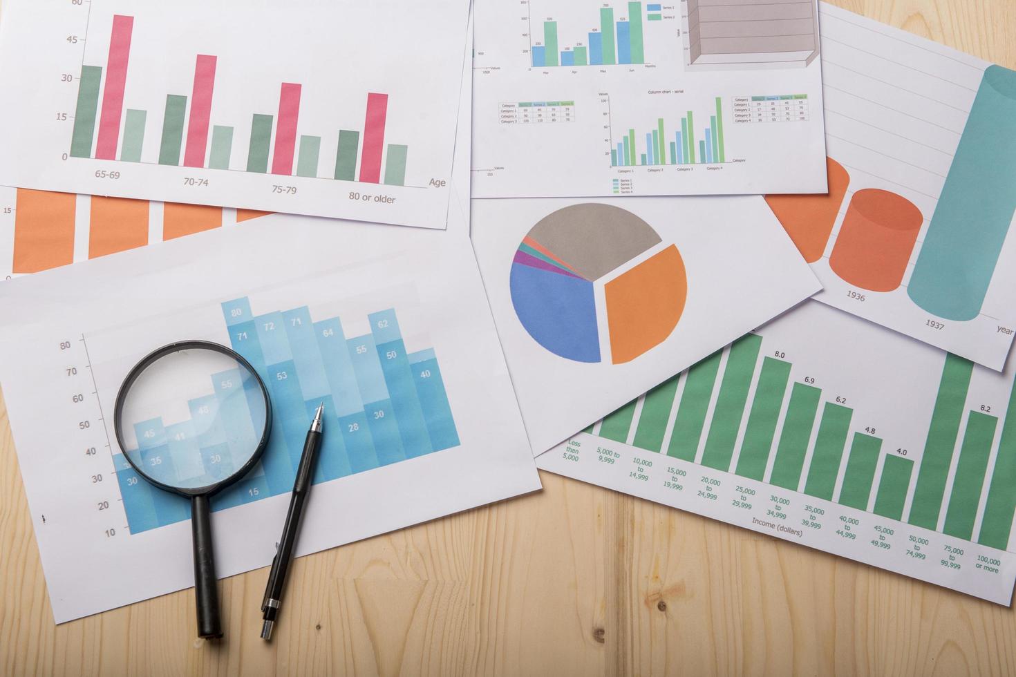 Magnifying glass and documents with analytics data lying on wood table photo