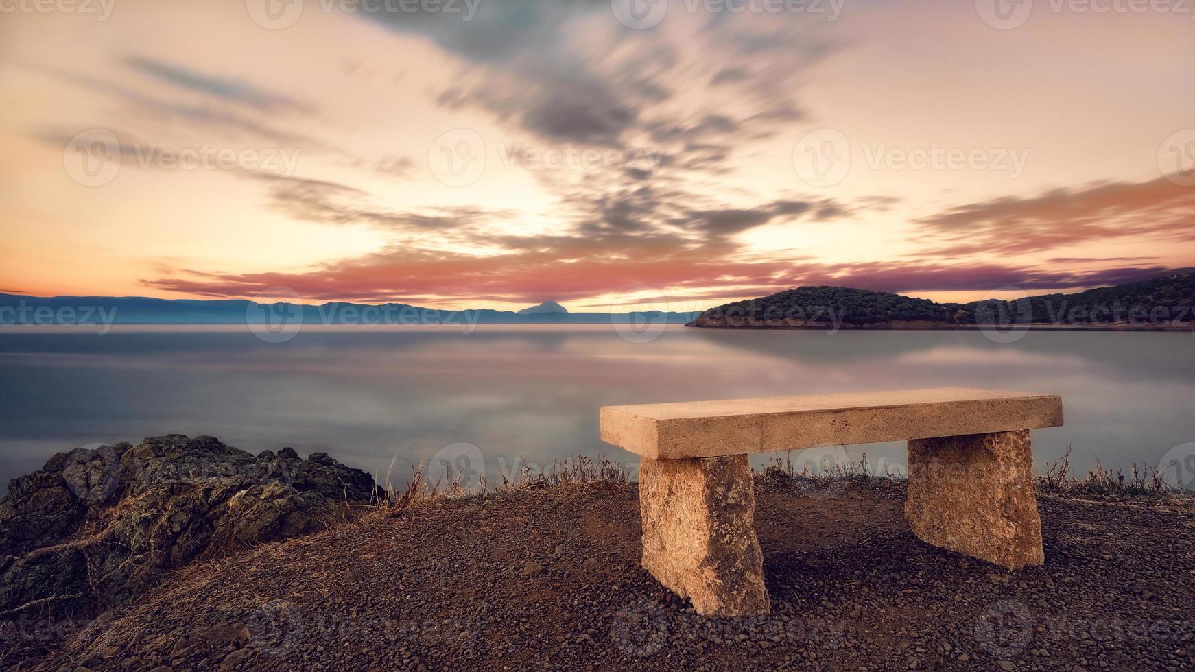 Stone bench at sunset. Beautiful sunset over the Aegean sea, Peninsula Kassandra, Halkidiki, Greece. On the horizon we see peninsula Sithonia and peninsula Athos behind. photo