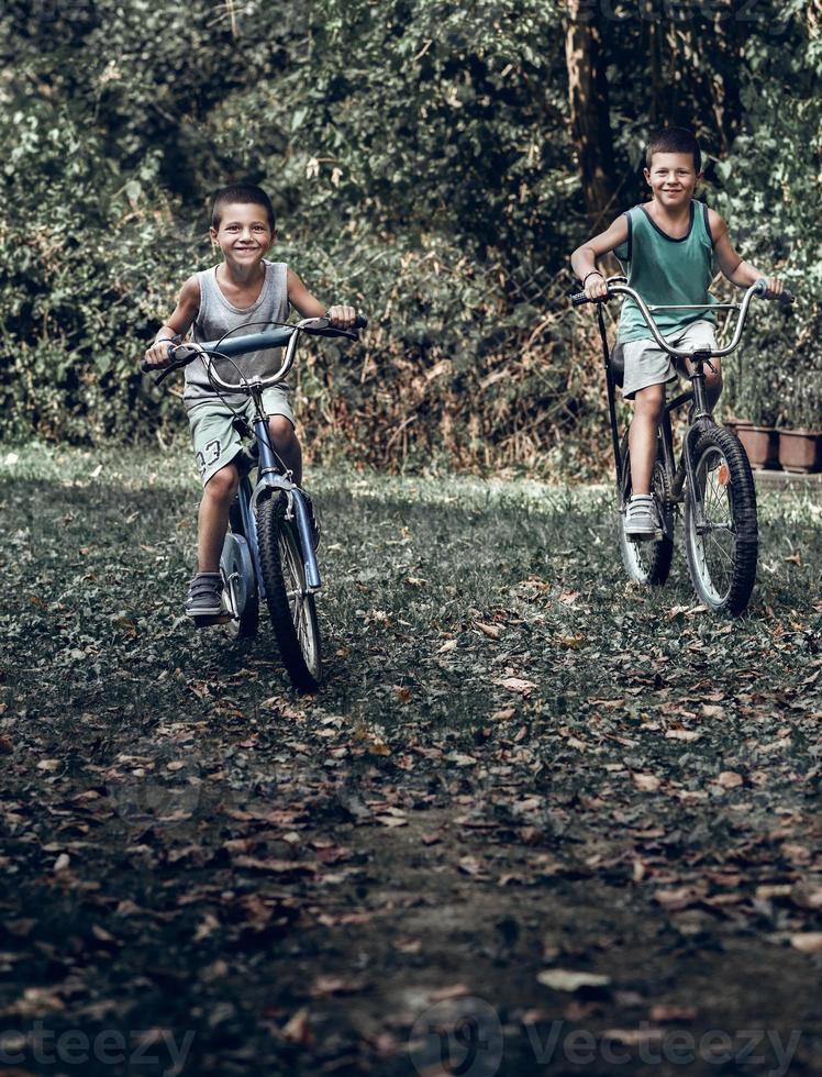 Two young boys riding old rustic bikes. Two boys rides old bicycle in the backyard and looking at the camera. photo