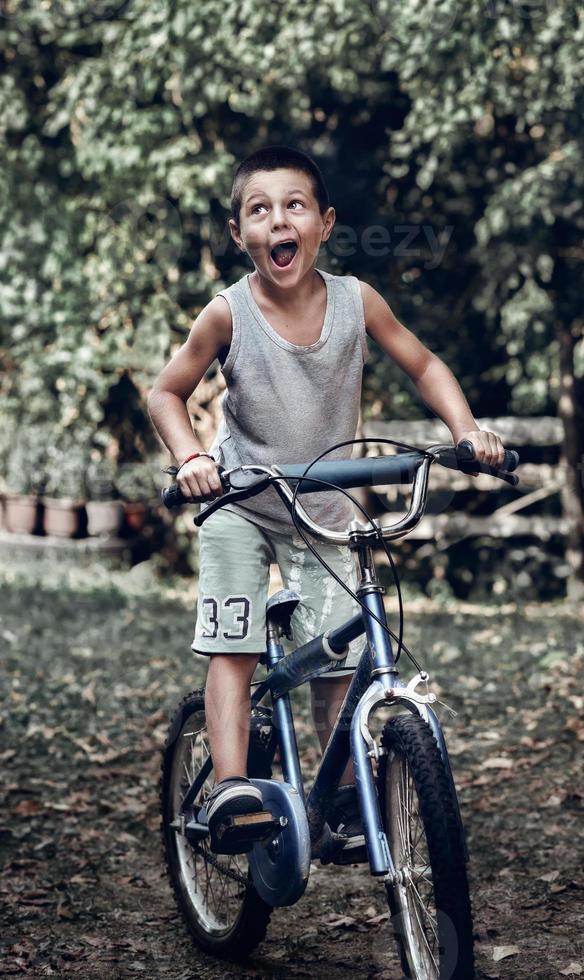 A boy with funny face riding his old rustic bike. A young boy rides his old bicycle in the backyard and makes a funny face. photo