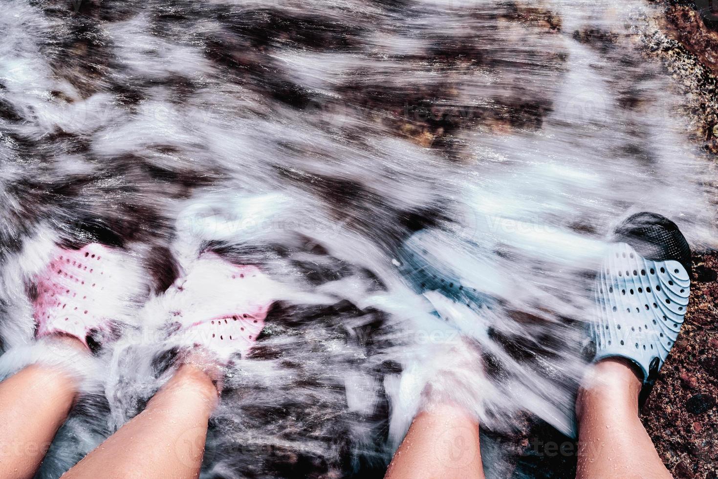 pareja de pie juntos en la orilla de piedra. pies de pareja cubiertos por olas de agua a la orilla del mar. foto