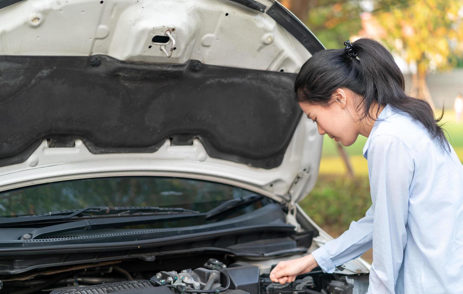 Mujer joven de pie cerca del coche averiado con el capó levantado que tiene problemas con su vehículo foto