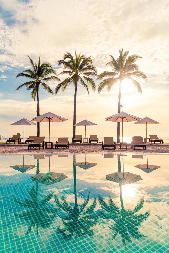 Hermosa sombrilla de lujo y una silla alrededor de la piscina al aire libre en el hotel y resort con palmera de coco en el cielo al atardecer o al amanecer foto