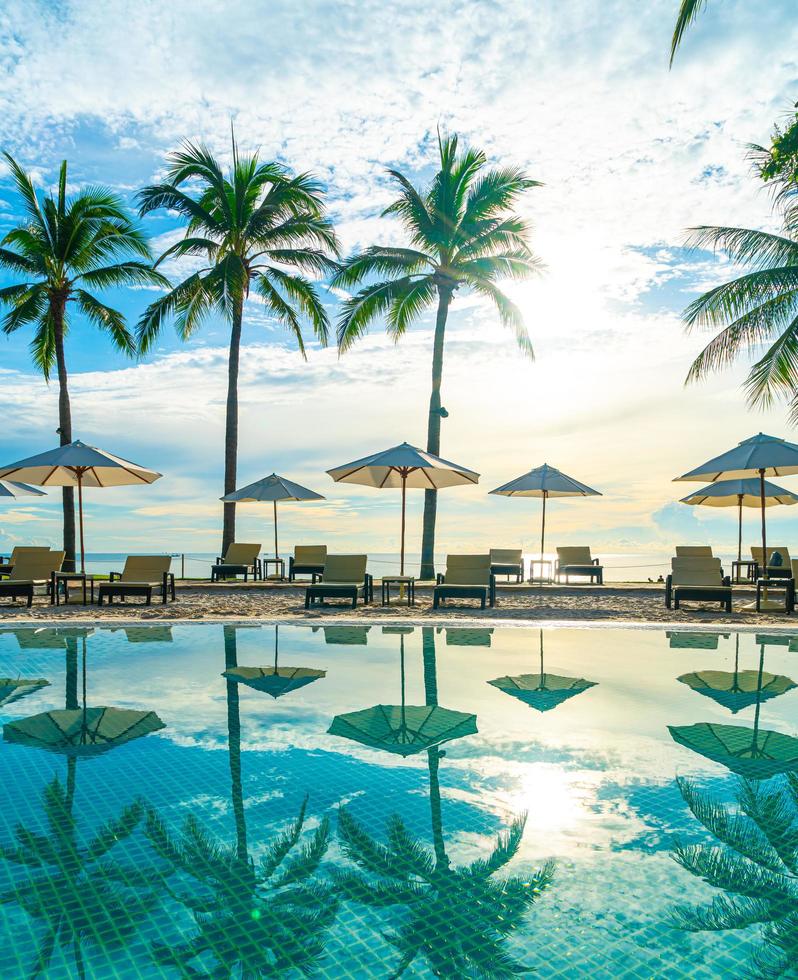 Hermosa sombrilla de lujo y una silla alrededor de la piscina al aire libre en el hotel y resort con palmera de coco en el cielo al atardecer o al amanecer foto