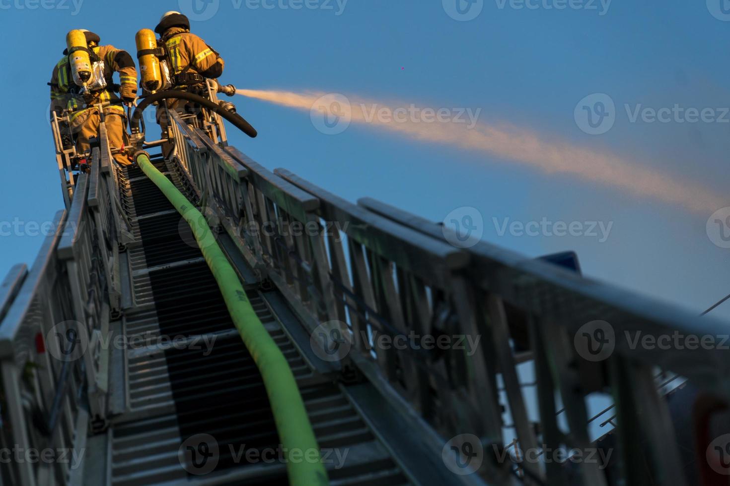 Firefighters climbing ladder against building and extinguishing a blaze photo