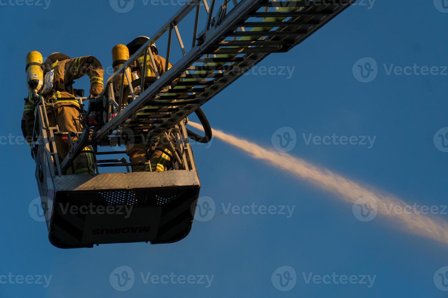 Firefighters climbing ladder against building and extinguishing a blaze photo