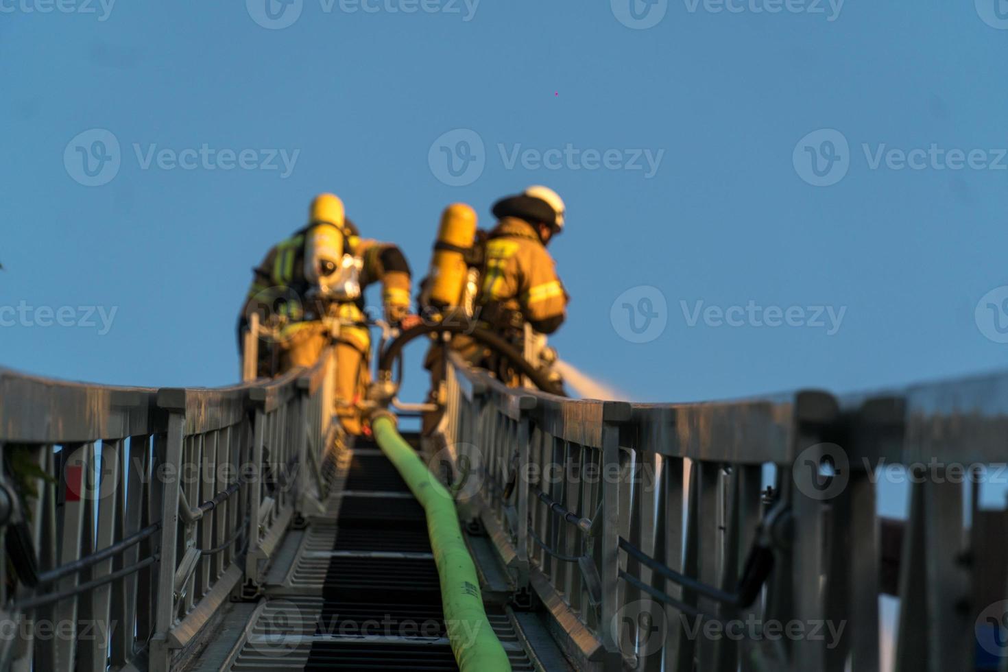 Firefighters climbing ladder against building and extinguishing a blaze photo