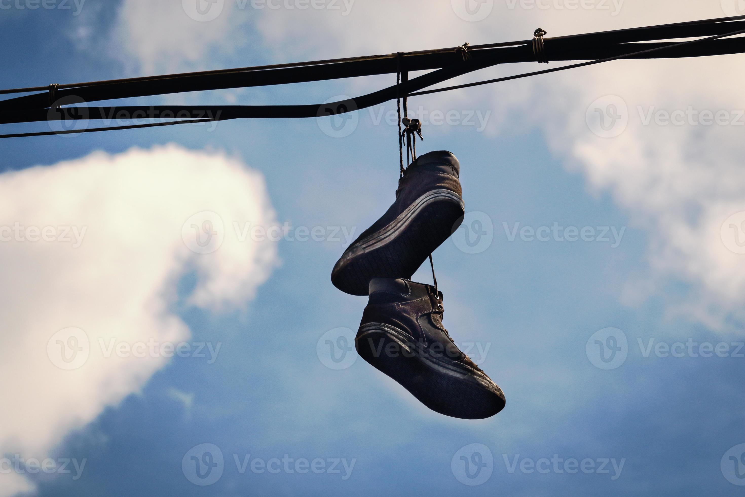 Two dirty old sneakers hanging on wires in blue sky with clouds 2623077