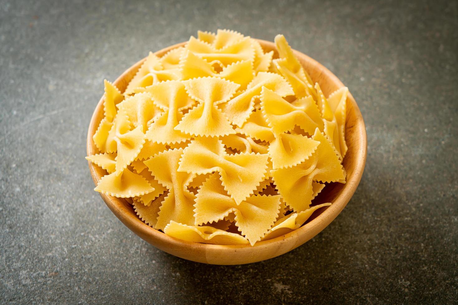 Secar la pasta farfalle cruda en un tazón de madera foto