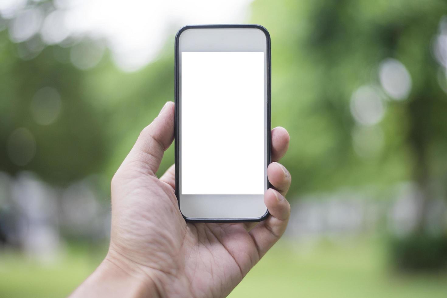 Cerrar la mano del hombre con el teléfono inteligente en el parque verde, maqueta de la pantalla en blanco del teléfono inteligente foto