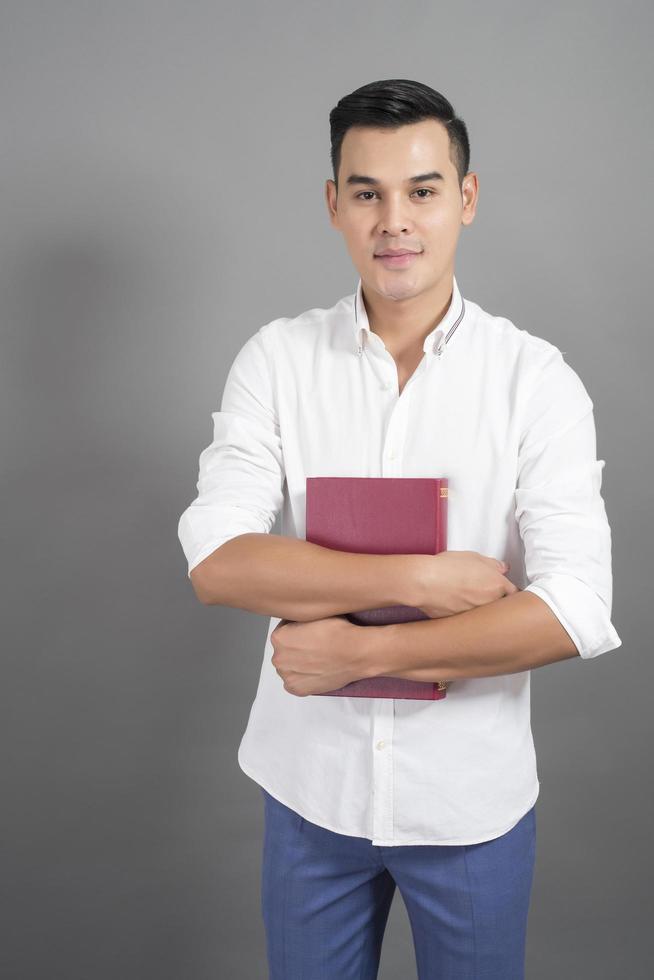 Retrato de hombre estudiante universitario sosteniendo el libro en el estudio de fondo gris foto