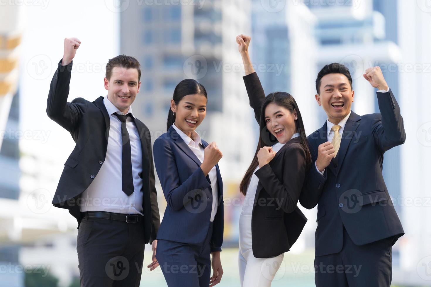 Cuatro ejecutivos seguidos, equipo empresarial de pie y vitoreando frente a la oficina moderna foto