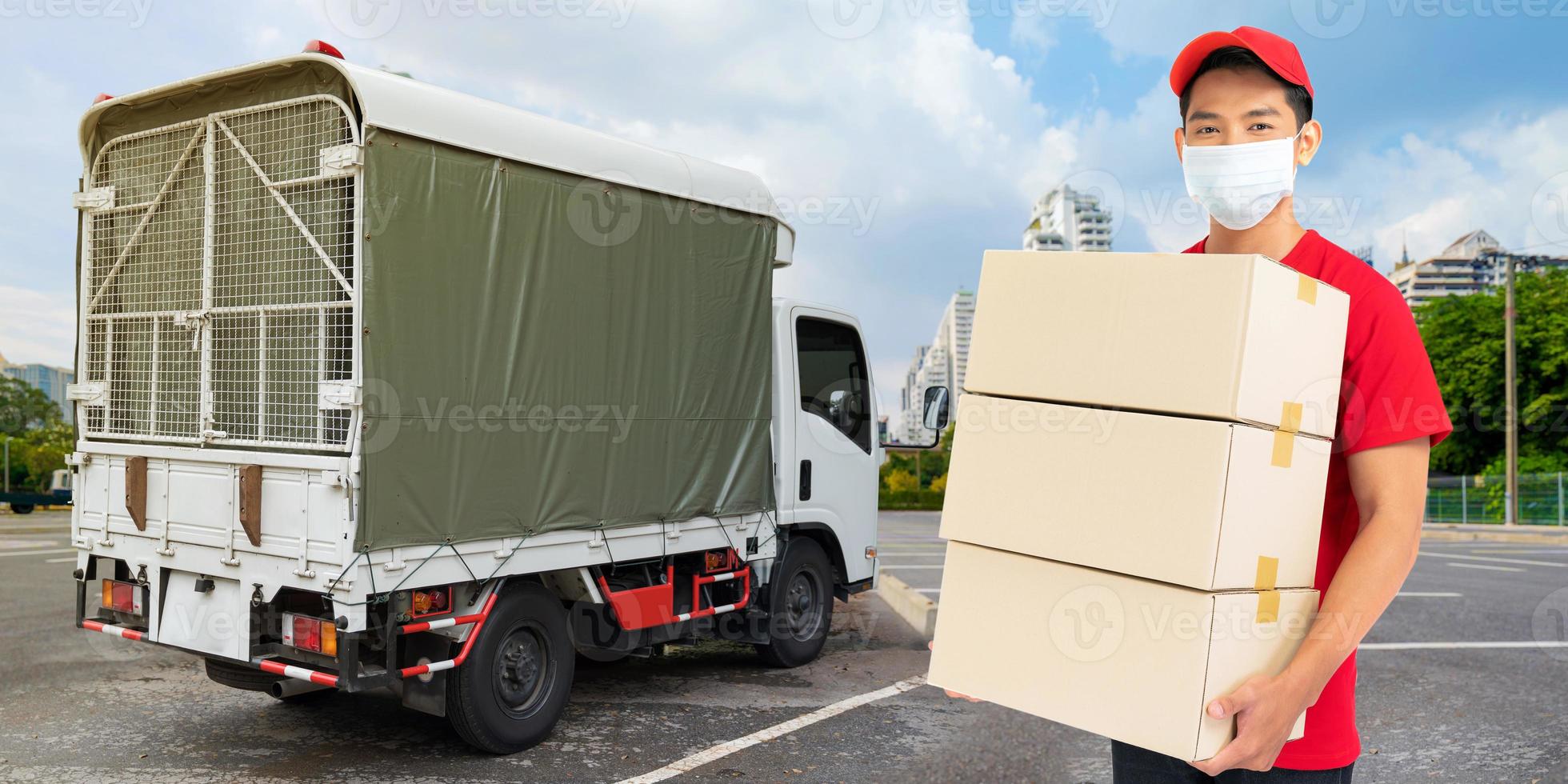 Delivery man employee in red t-shirt uniform face mask holding empty cardboard box photo