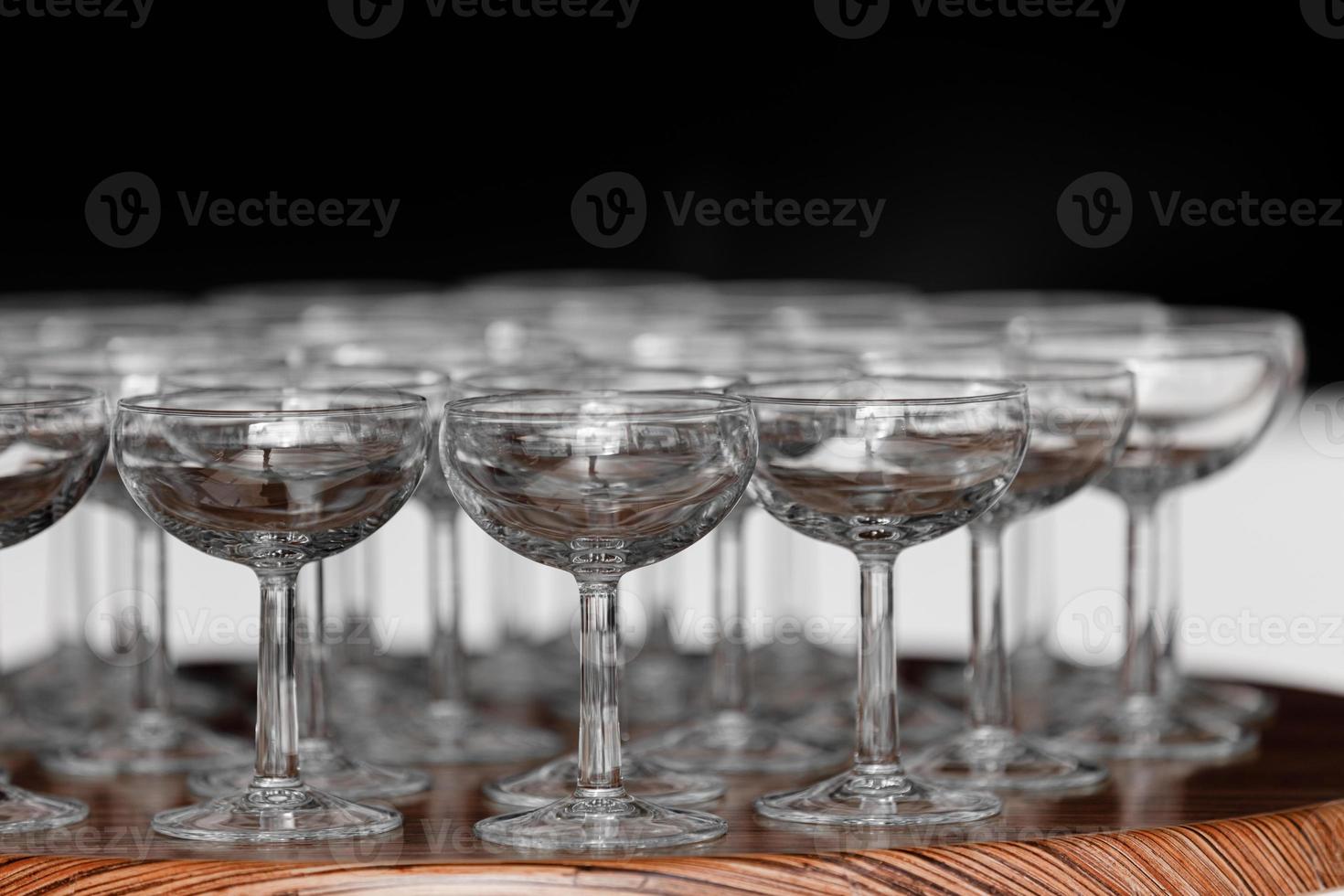 muchas elegantes copas vacías de vino o champán en la mesa de madera en el día de la boda. conjunto de vasos vacíos en blanco que se muestran en filas. preparación para las vacaciones foto