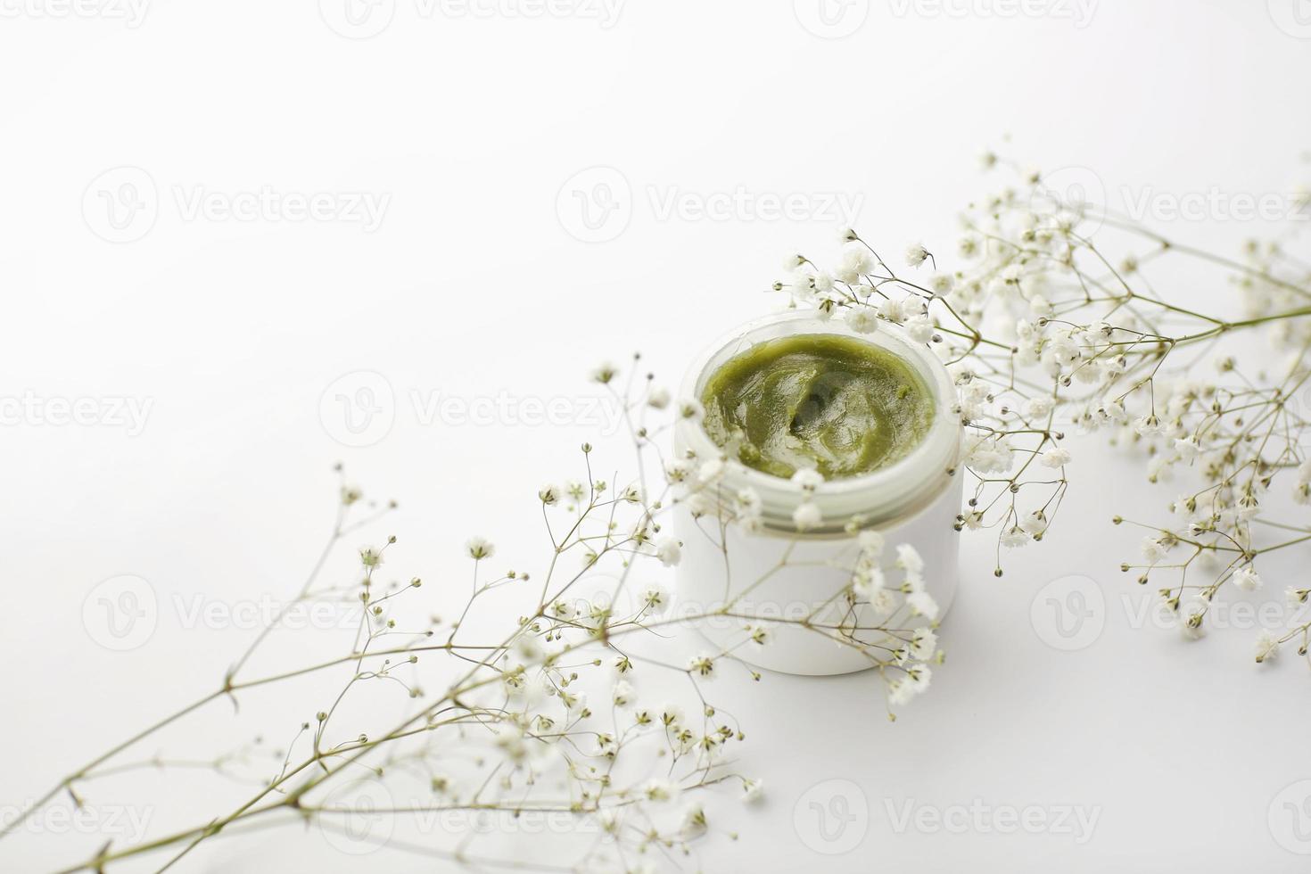 Envase de plástico abierto con crema y flores sobre un fondo blanco. crema facial. crema de hierbas. productos cosméticos. enfoque selectivo. foto