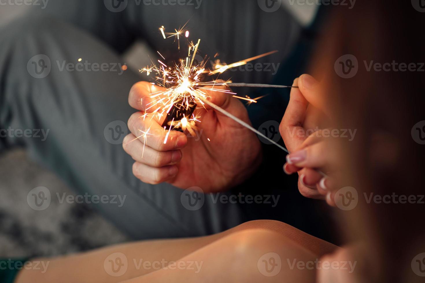 pareja sosteniendo luz de bengala. manos masculinas y femeninas sostienen luces de bengala encendidas. hermosa familia joven feliz celebrando la Navidad juntos. foto