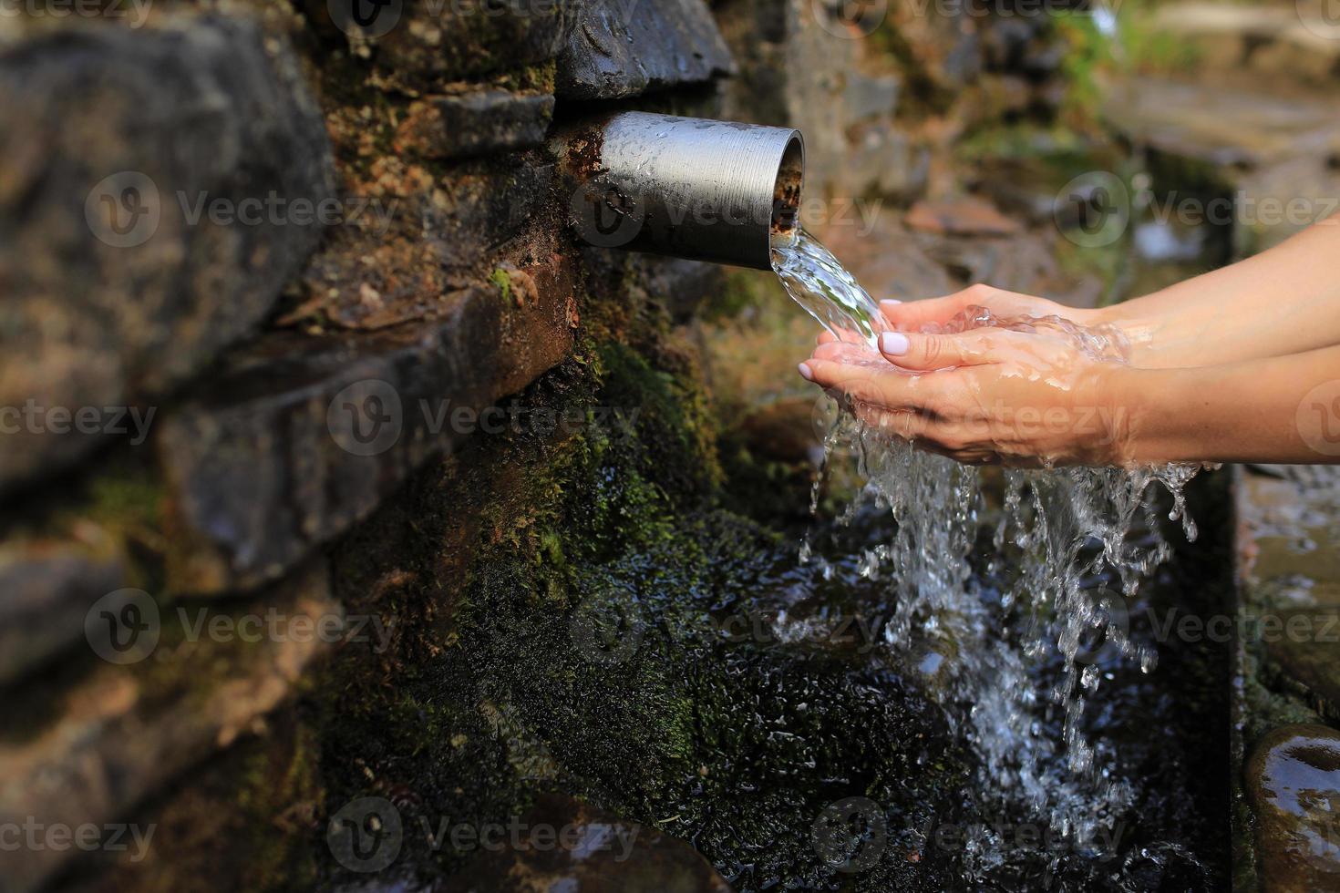 Woman collect pure water in hand palm from the source in the wall, hold and drink it. Female hand scooping spring water from the stone in forest photo