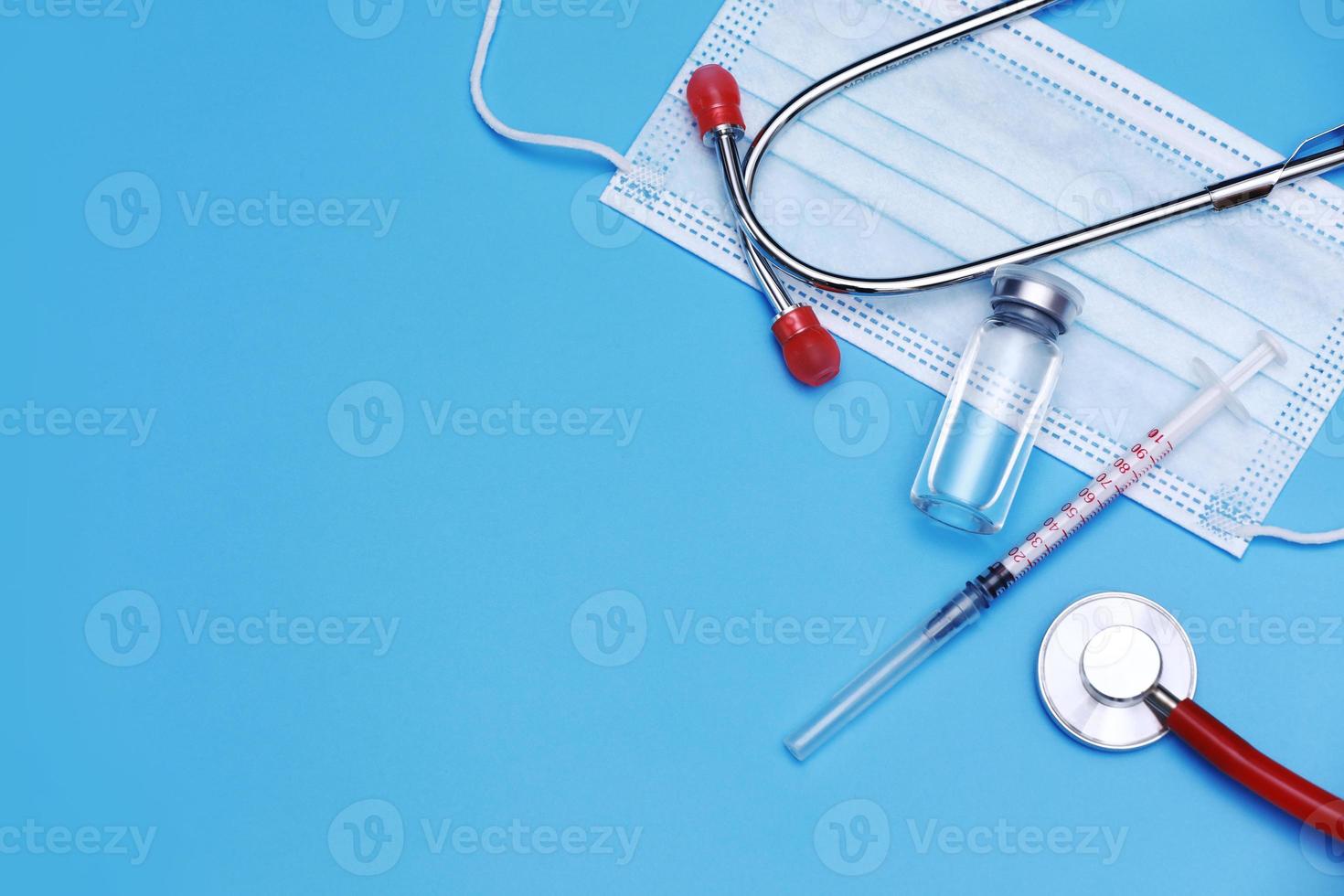 Medical bottle, vial, syringe, stethoscope and face mask on blue background with copy space. Vaccination session and immunity improvement. photo