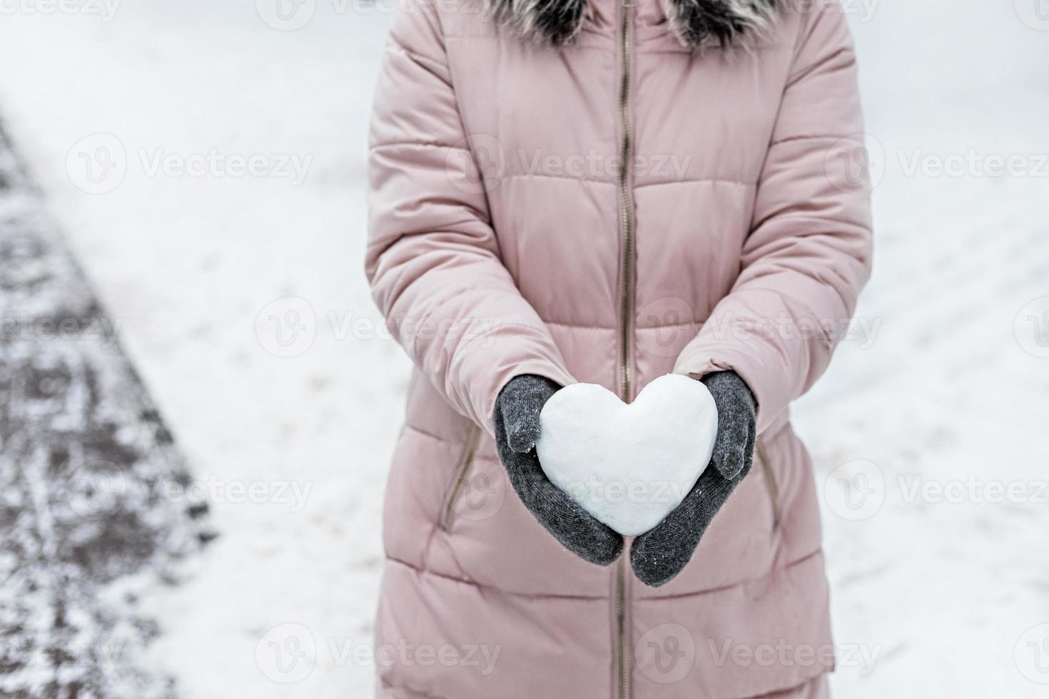 Women's hands in warm gray mittens with a snowy white heart. The Concept Of Valentine's Day photo