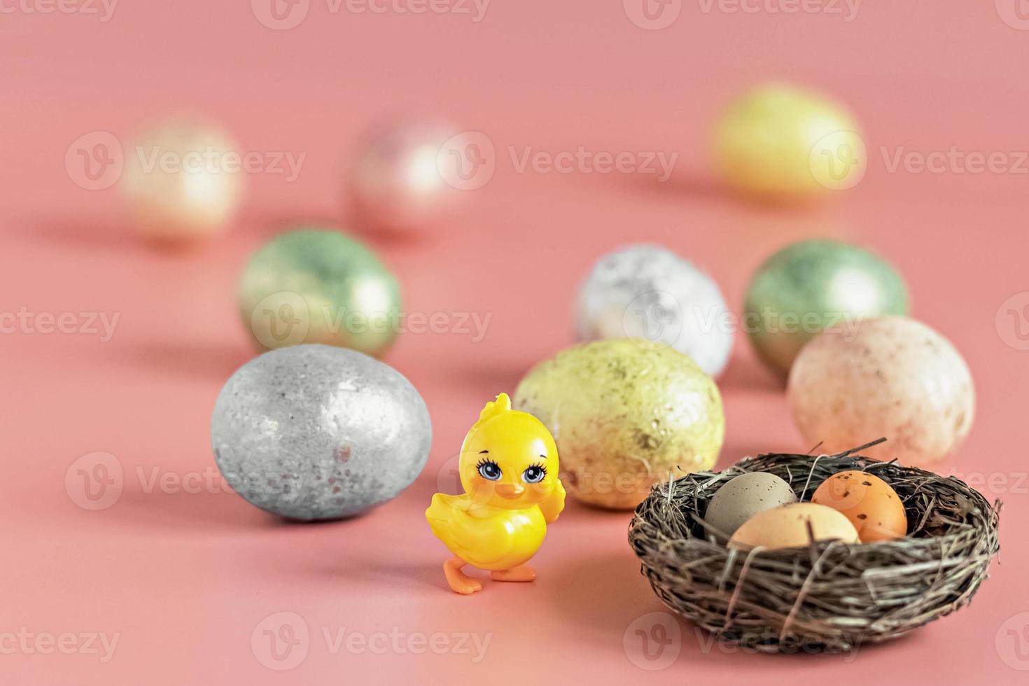 Easter eggs in a natural nest with bird eggs. Painted eggs and a decorative chicken on a pink background of pastel colors. Selective focus photo