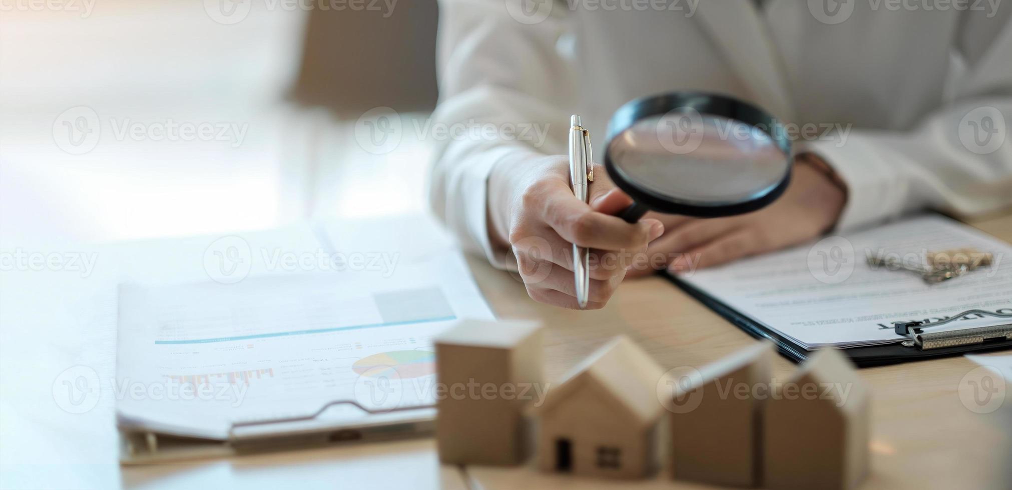 Hand holding magnifying glass and looking at house model, house selection, real estate concept. photo