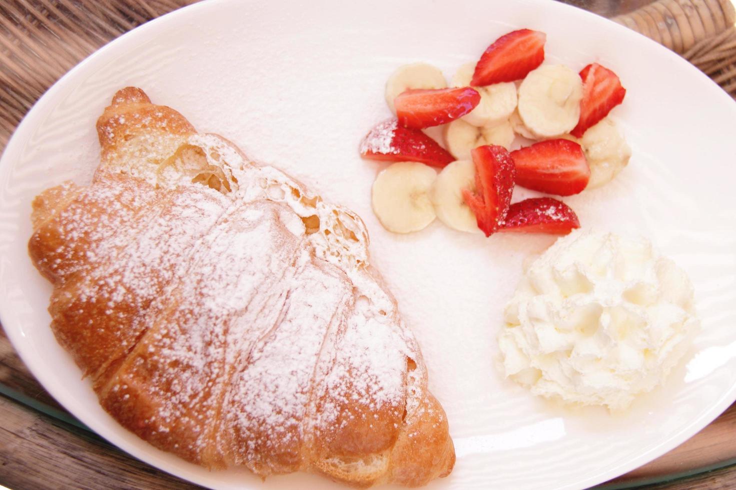 cut fresh strawberry and banana with roll and cream on plate for breakfast photo