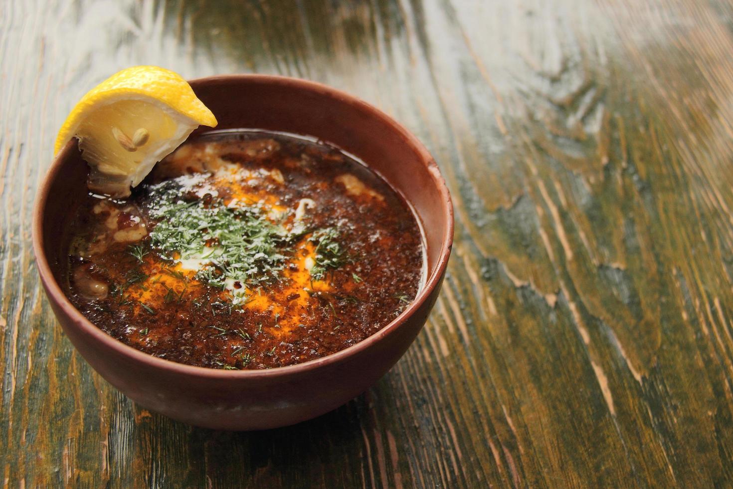 Sopa de tomate solyanka con rodaja de limón en cuenco de barro foto