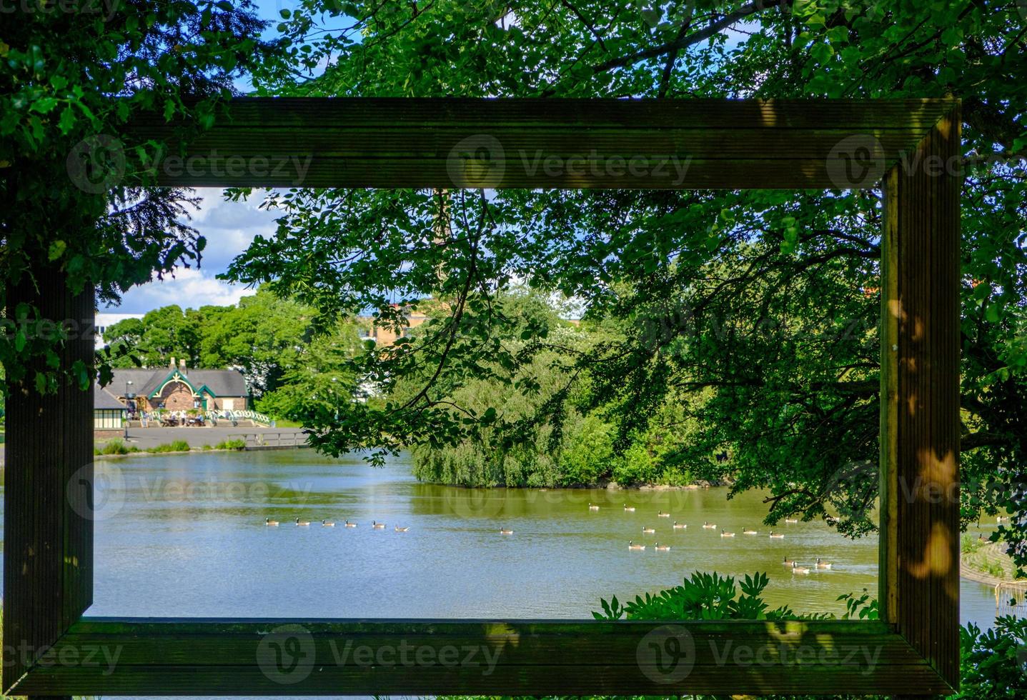 View through large hollow picture frame of trees and birds in pond photo