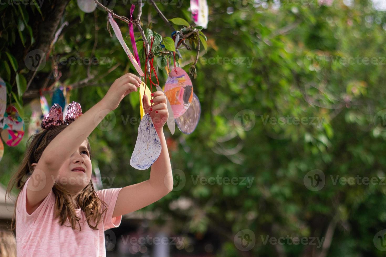 linda niña colgando del árbol sus tarjetas de pascua en forma de huevo, para buena suerte y con buenos deseos foto