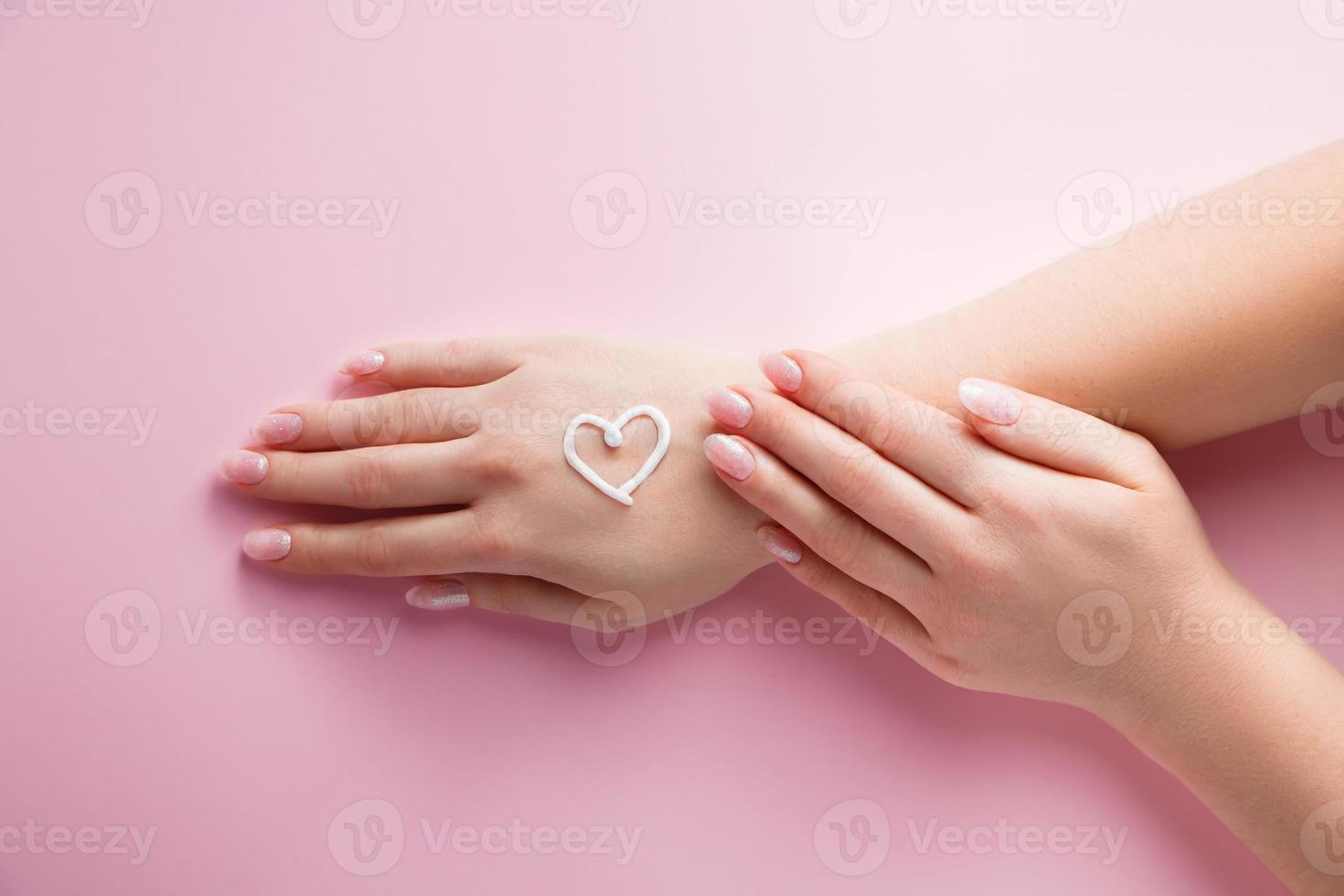 concepto de cuidado de la piel. mujer se está aplicando crema en las manos sobre fondo rosa. imagen para publicidad y diseño. foto