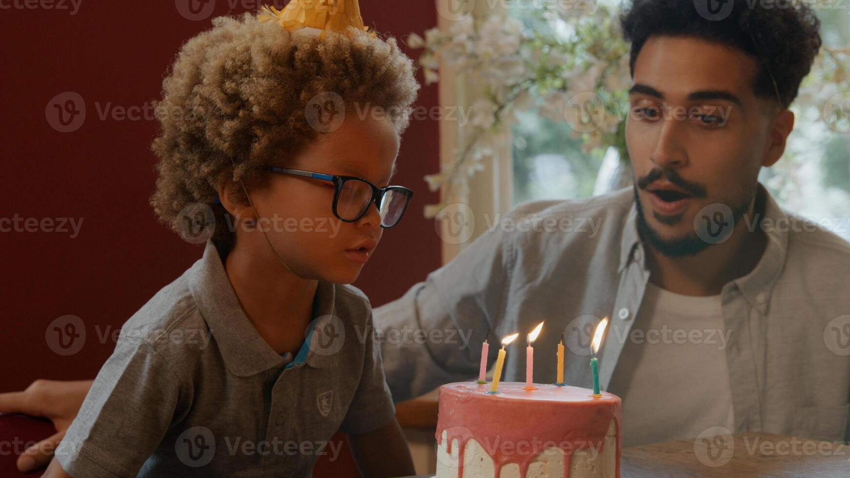 Boy blowing out candles on cake with family watching photo