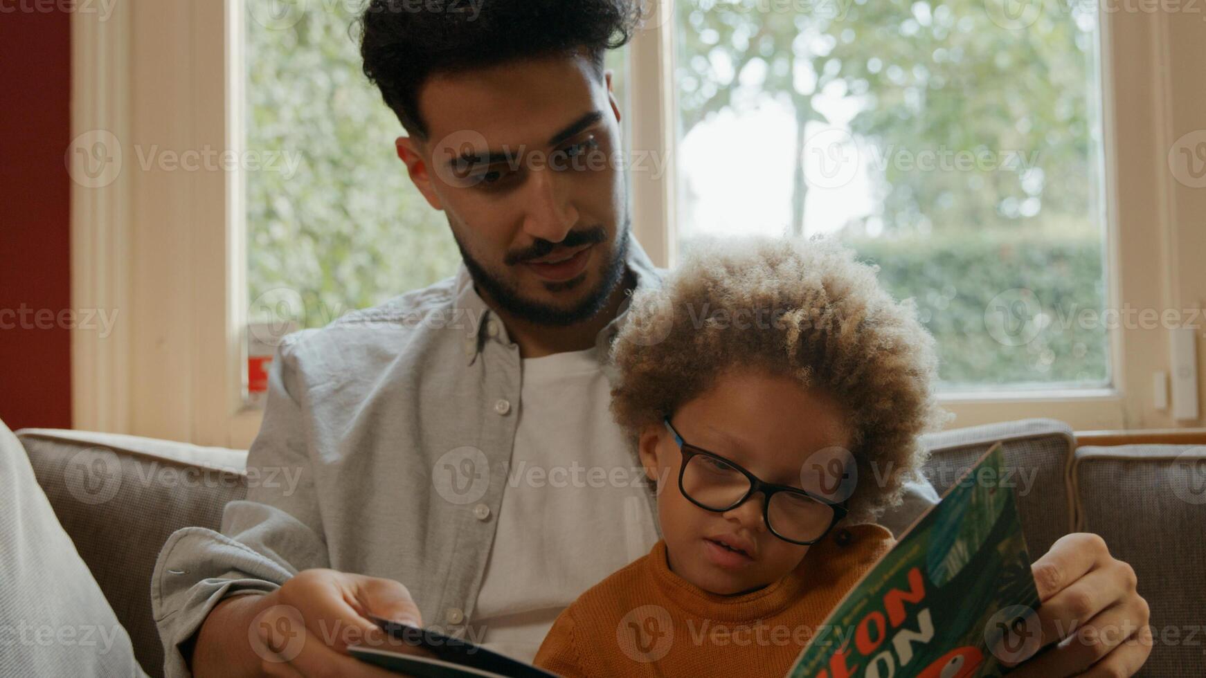 Young boy reading book to father at home photo