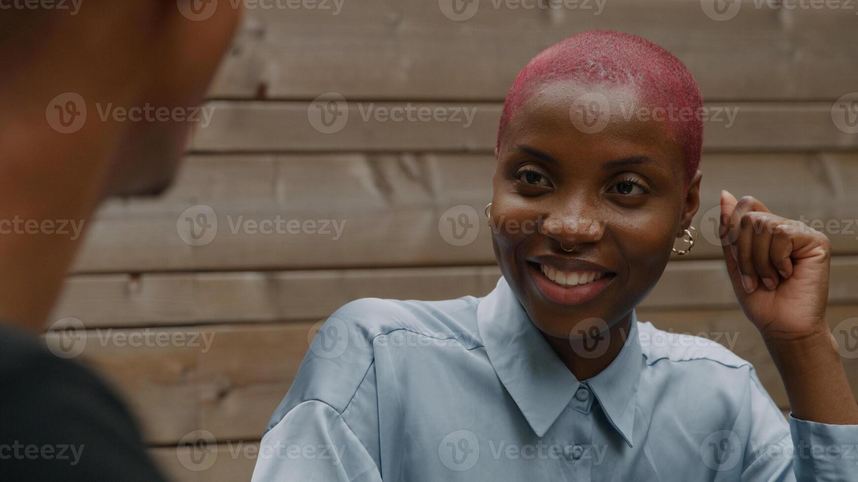 Young woman with shaved pink hair listening to colleague photo