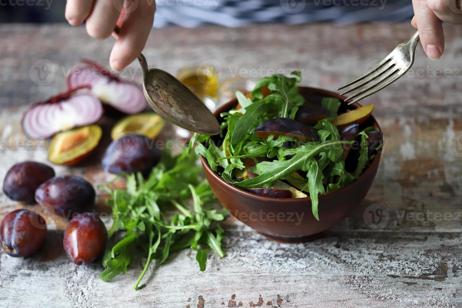 Ensalada saludable mezclar manos masculinas con cuchara y tenedor. ensalada de rúcula y ciruela. foto