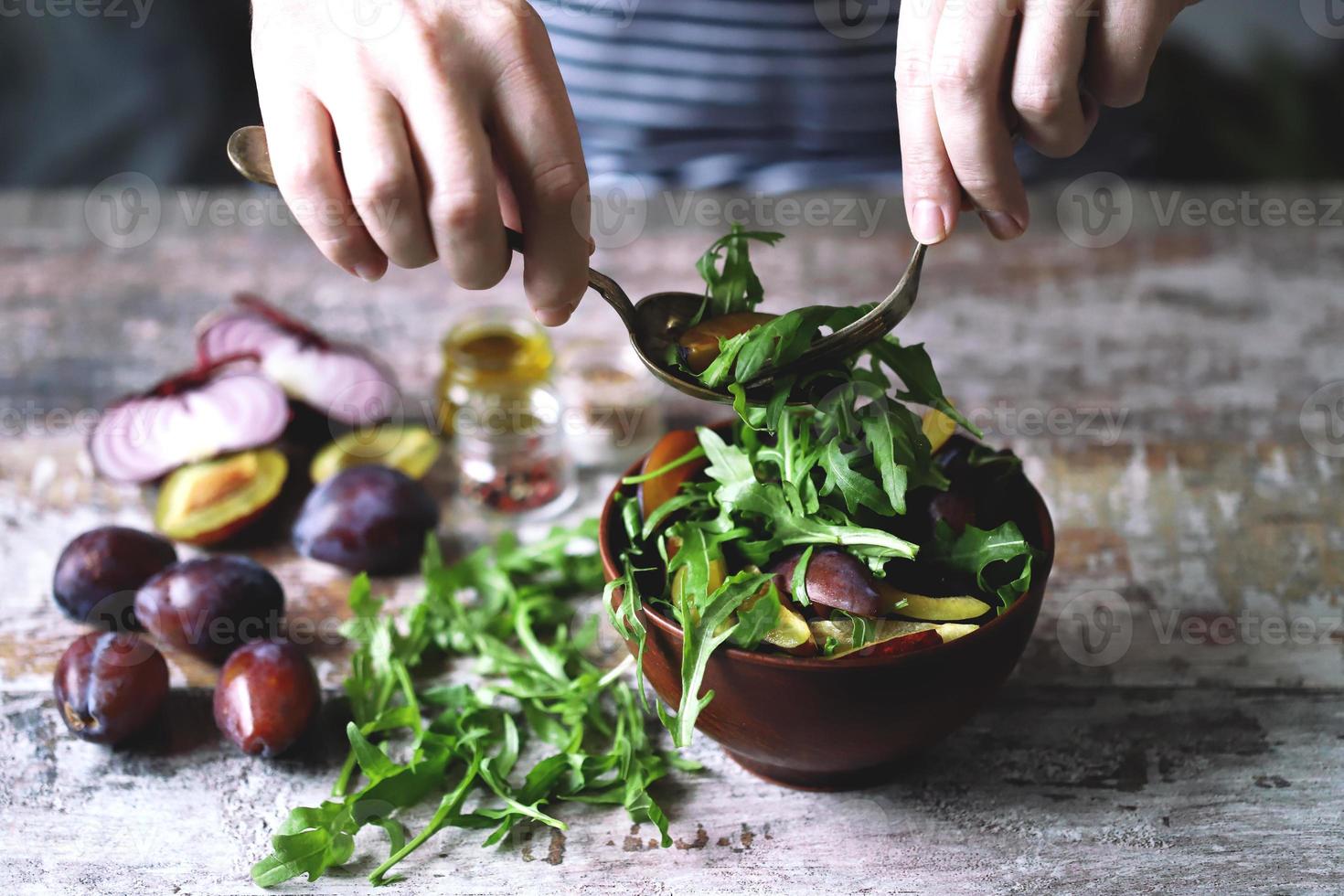 Ensalada saludable mezclar manos masculinas con cuchara y tenedor. ensalada de rúcula y ciruela. foto