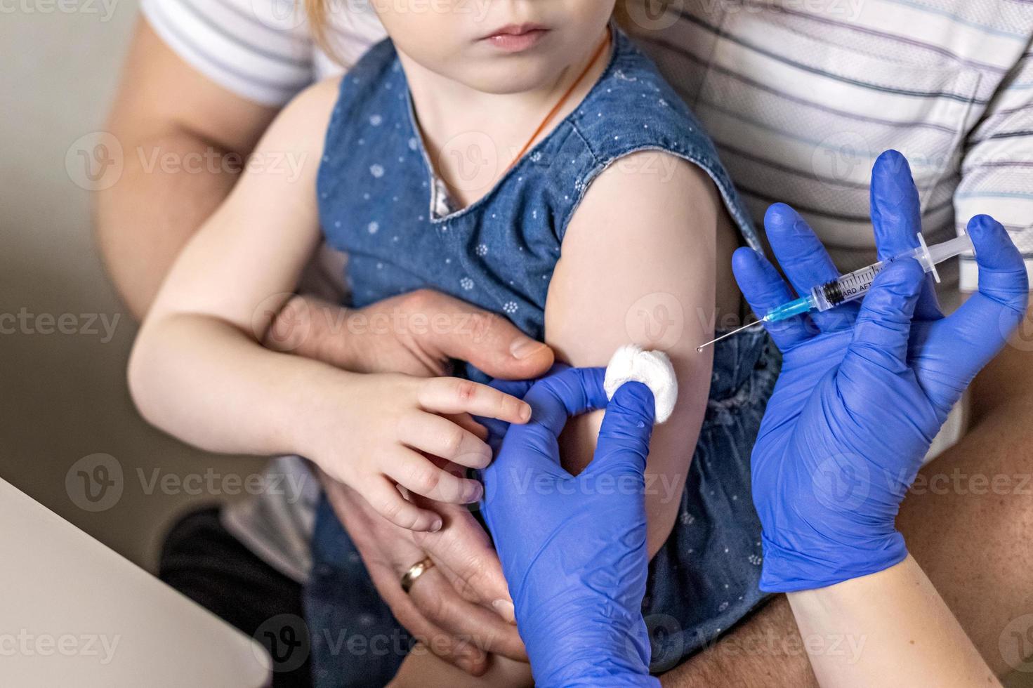 una niña con su padre en el consultorio del médico en la clínica está siendo vacunada contra el coronavirus. el concepto de vacunación, inmunización, prevención contra el covid-19. foto