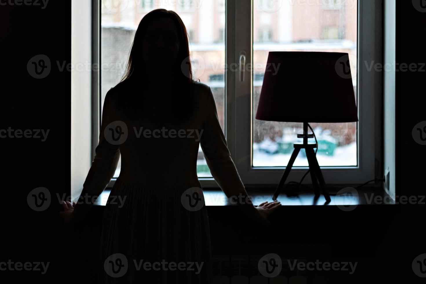 silueta de una mujer joven en la ventana. lámpara vintage en el alféizar de la ventana foto