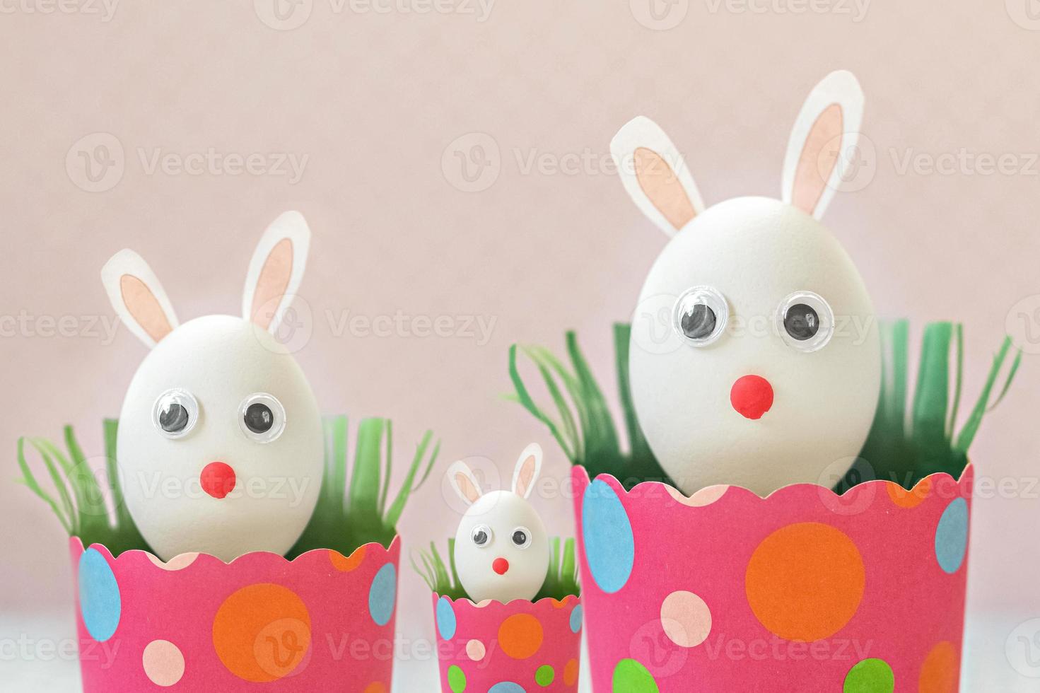 huevos de gallina blanca con orejas de conejo en bandejas de papel rosa ecológicas, cajas. familia feliz concepto de vacaciones de pascua. foto